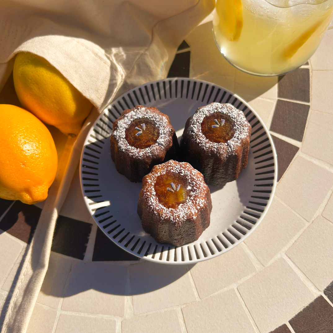 Three small round pastries on a plate with a glass of lemonade and lemons on a stone surface.