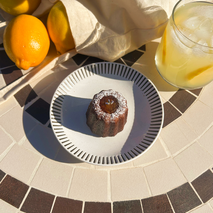 Canele on a plate with lemons and a glass of lemonade on a tiled surface